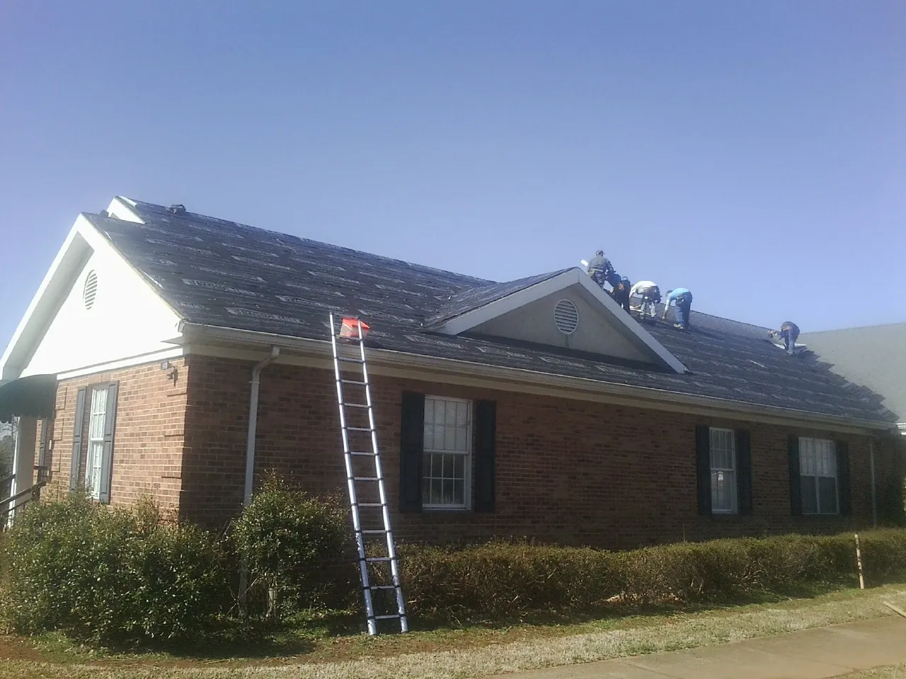 Crew tearing shingles off a brick ranch roof with a ladder set — Emergency Roof Repair work by our crew in Newfields