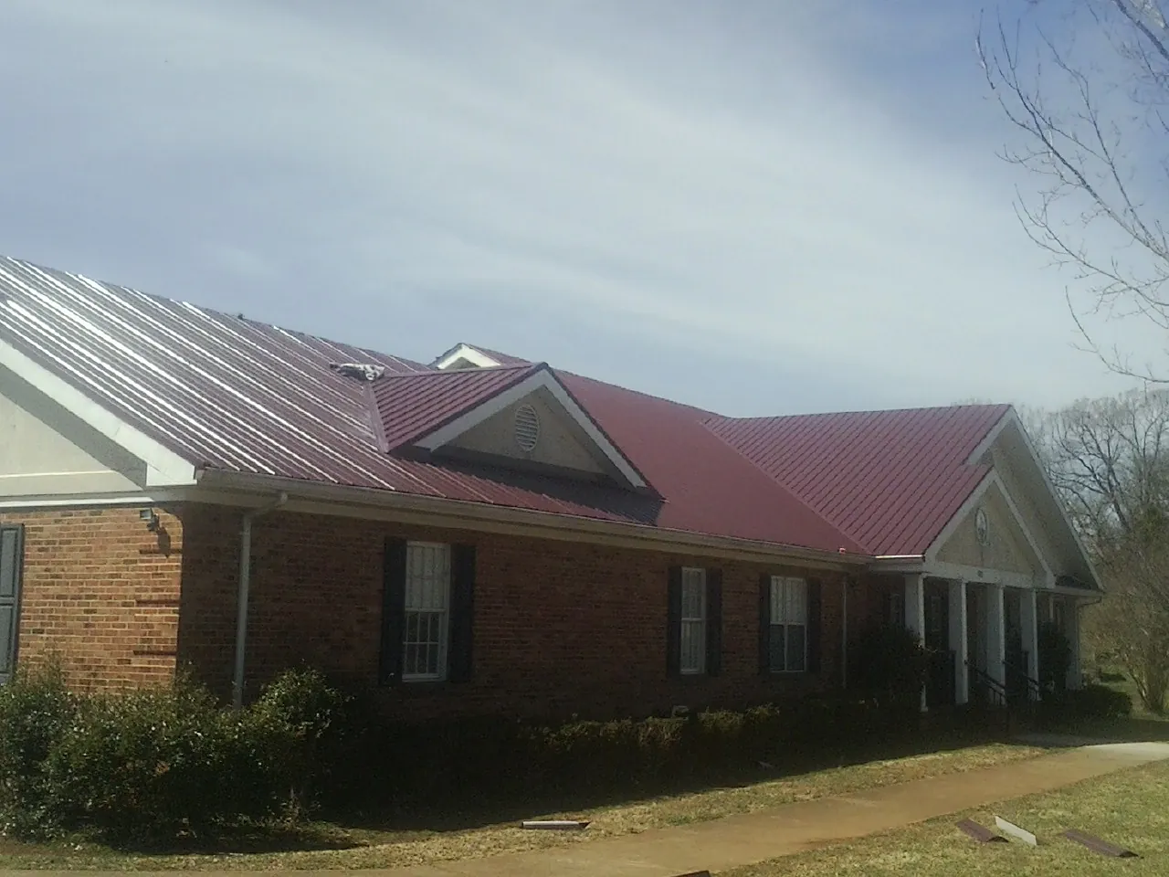 Red metal roof with gabled entries on a long brick building, from a Hail Damage Roof Repair job in Newfields