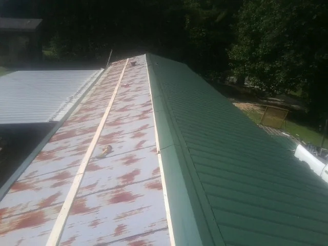 Old rusted panels beside newly installed green metal roofing — Wind Damage Roof Repair by Roofing Brothers in Newfields