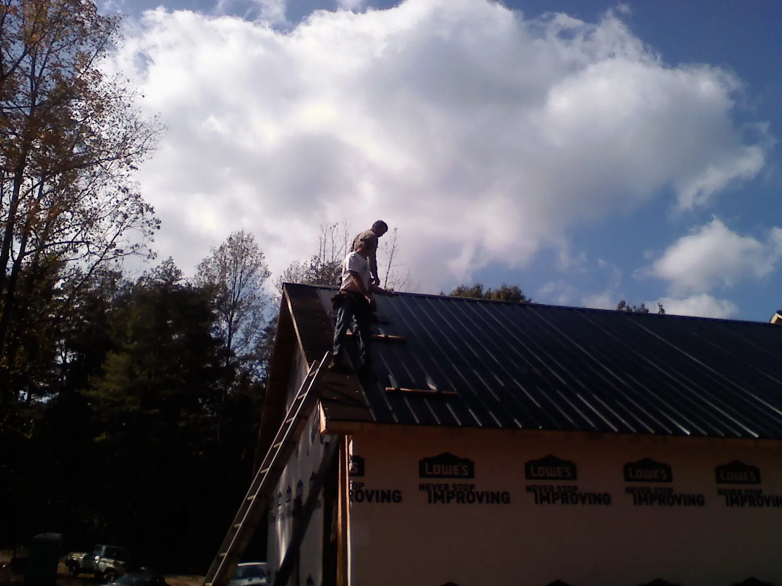 Roofer fastening dark metal panels high against a cloudy sky, from a Roof Inspection job in Newfields