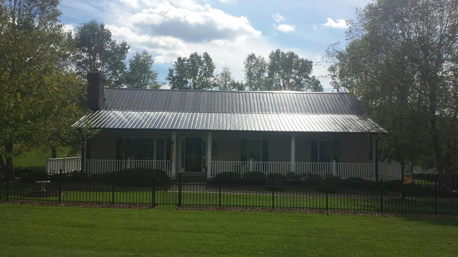 Gray metal roof on a brick ranch with a full width front porch — Gutter Guard Installation work by our crew in Newfields