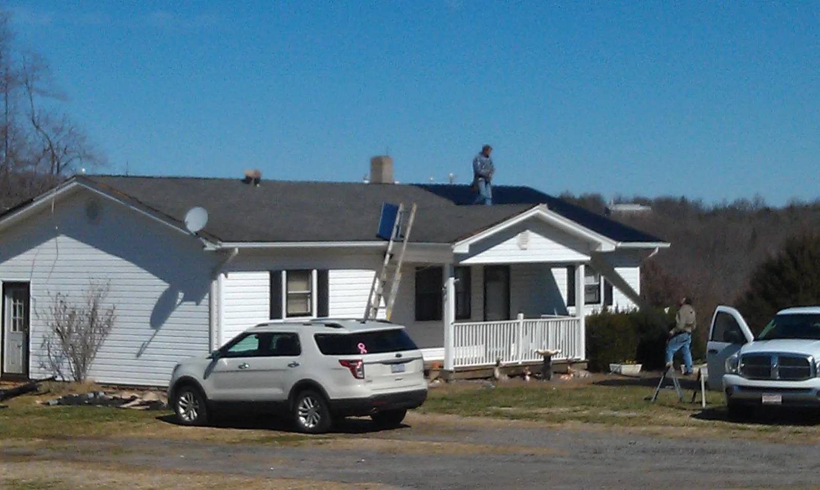 Roofers stripping shingles from a white ranch house roof in Newfields