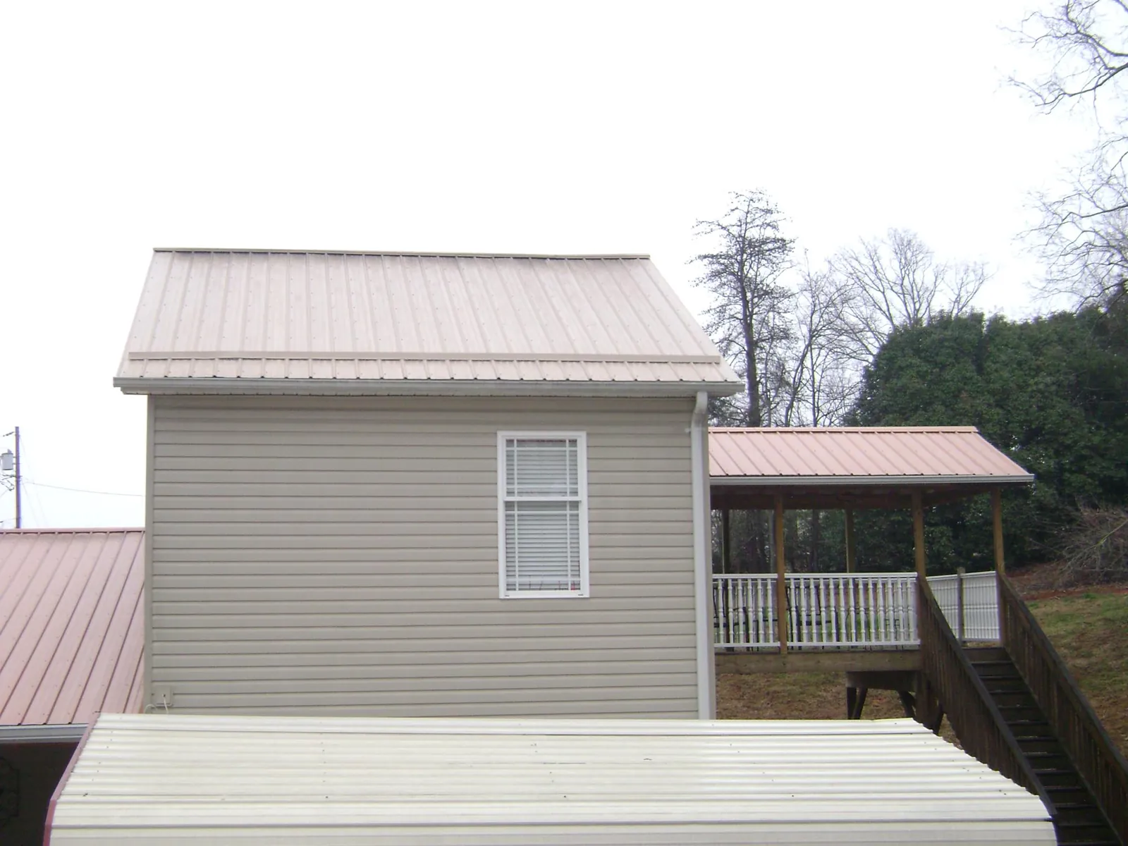 Tan metal roofs on a two story addition and attached porch, from a Roof Replacement job in Newfields